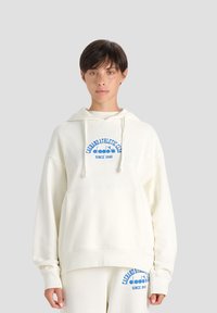 Felpa crema con tasca frontale, cappuccio con cordoncino e testo grafico blu. Etichettata "GARELLO ATHLETIC CAMPS diadora SINCE 1948." Tessuto morbido.