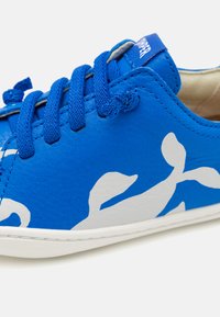 Sneaker blu in pelle con design astratto bianco, dotato di lacci blu, colletto imbottito e suola in gomma bianca.
