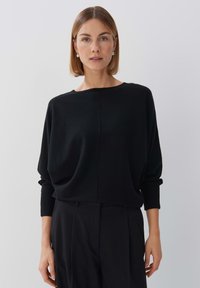 Schwarzer Strickpullover mit rundem Halsausschnitt und abgesenkten Schultern. Hat eine lockere Passform und lange Ärmel, gefertigt aus weichem, strukturiertem Material.