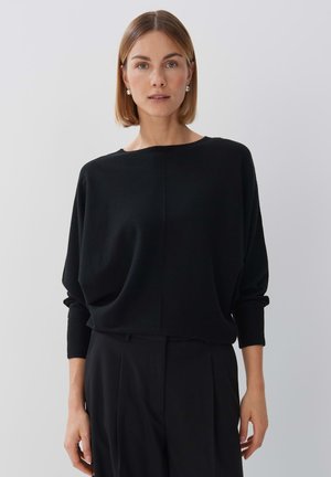 Pull-over en tricot noir avec un col rond et des épaules tombantes. Il présente une coupe décontractée et des manches longues, fabriqué dans un matériau doux et texturé.