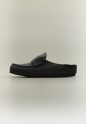 Zwarte slip-on loafer met een platte rubberen zool en gestikte details, gefotografeerd van de zijkant op een neutrale achtergrond.