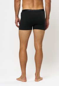 Črne bombažne bokserice s enotno zasnovo, ki imajo pas z logotipom Kappa. Prilegajo se tesno okoli stegen in nog.