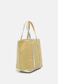 Beige canvasbärväska med silverkant på handtagen och basen, visad i en lätt vinkel mot en vit bakgrund.