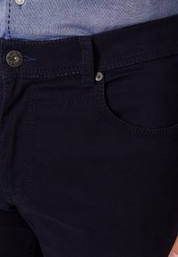 Pantaloni di cotone blu navy con una texture liscia, design a cinque tasche e cuciture a contrasto. Caratterizzati da una chiusura con bottone e dettagli in metallo.