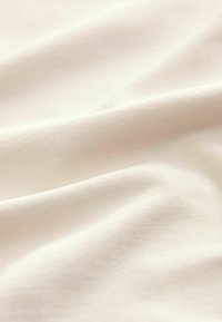 Weiches, cremefarbenes Gewebe mit einer glatten Textur, das subtile Rippungen und sanfte Falten aufweist, geeignet für Kleidung oder Polsterung.