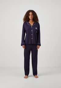 Set de pijamale bleumarin cu cămașă cu mânecă lungă și nasturi și pantaloni asortați. Are tiv alb și un mic logo brodat pe piept.