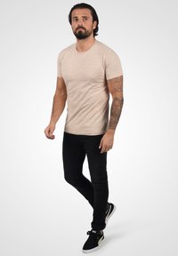 Camiseta ajustada beige claro con un patrón texturizado, combinada con unos jeans negros de corte slim y zapatos negros con detalles dorados.
