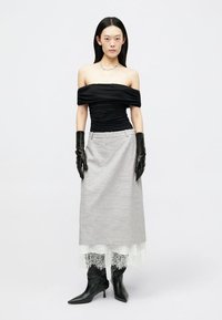 Juodas off-shoulder viršus, pilkas sijonas su nėrinių apdaila, juodos pirštinės ir smailūs ankle batai. Lygus audinio tekstūra ir modernus dizainas.