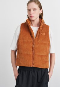 Puumähibest burnt orange värviga, kõrge kraega, tõmblukuga ja kvaliteetse tekstuuriga. Omab logot ja küljetaskuid. Kandmine valge särk üle.