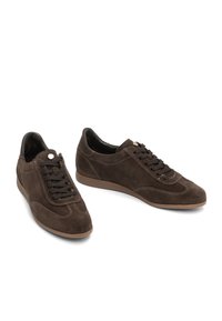 Un paio di scarpe casual in suede marrone scuro con lacci, suole in gomma marrone chiaro, cuciture dettagliate e un piccolo accento metallico sulla linguetta.