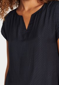 Blouse marine avec un décolleté en V et des manches courtes, présentant un motif texturé subtil de petits points et un tissu doux.