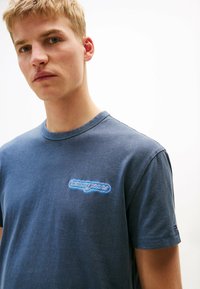 Camiseta de algodón azul marino con cuello redondo, mangas cortas y un colorido logo bordado de "Tommy Jeans" en el pecho.