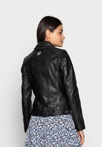 Zwarte leren jas met een getailleerd ontwerp, voorzien van een ritssluiting, schouderstukken en een logo-embleem op de achterkant. Hoogwaardige, gestructureerde stof.