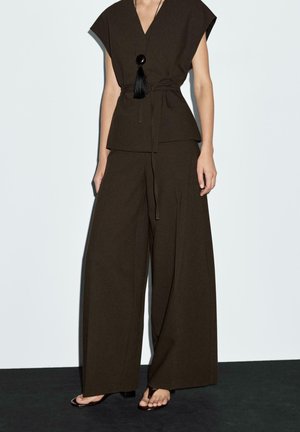 Pantalons marron à jambes larges associés à un haut assorti à manches courtes avec un décolleté en V et des détails en franges noires. Design épuré et minimaliste.