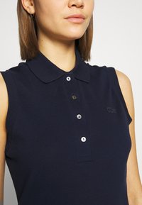 Mornarsko brezrokavno polo majico, teksturirana tkanina, s klasičnim ovratnikom in placketom s tremi gumbi z metalik gumbi; logo na levi prsni strani.