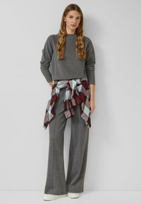 Szara krótka bluza zestawiona z szerokimi szarymi spodniami. Koszula flanelowa w kratę, zawiązana w talii, w bordowo-niebieskie akcenty. Białe trampki.