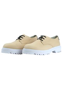 Beige leren schoenen met zwarte veters, ronde neus en witte rubberen buitenzool met opvallende profielgroeven voor grip.