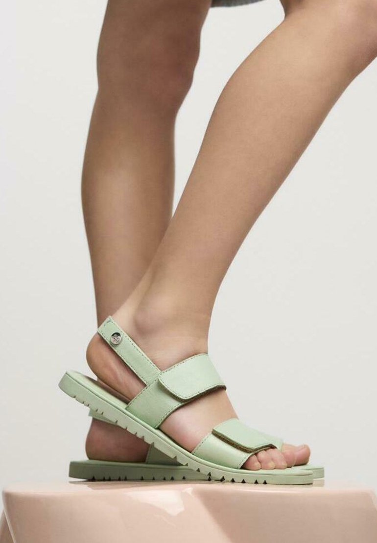 Sandali verde chiaro con design a punta chiusa, cinturini regolabili e suola texturizzata, posizionati su uno sfondo neutro.