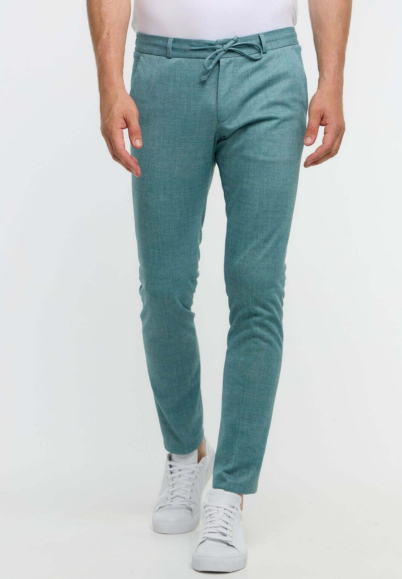 Helle türkisfarbene Slim-Fit-Hosen aus weichem Stoff, mit einem Kordelzugbund und einer subtilen Textur. Kombiniert mit weißen Sneakers.