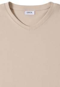 T-shirt beige à col en V en coton doux. Le tissu a une texture lisse avec des bords cousus et une petite étiquette portant la mention "CECIL".