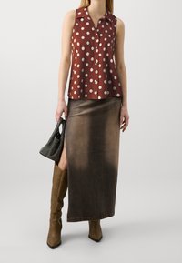 Top rojo sin mangas con lunares blancos y un collar, combinado con una falda maxi de degradado marrón. Bolso negro texturizado y botas hasta la rodilla.