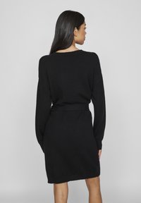 Μαύρο πλεχτό φόρεμα με μακριά μανίκια, χαλαρή εφαρμογή και δεμένο στη μέση. Διαθέτει στρογγυλή λαιμόκοψη και μαλακή υφή.