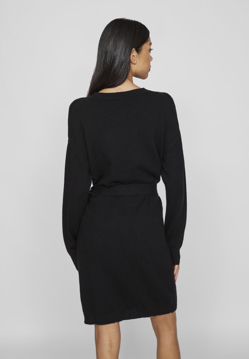 Schwarzes gestricktes Kleid mit langen Ärmeln, lockerer Passform und gebundenem Taillengürtel. Merkmale sind ein gerundeter Halsausschnitt und weicher Stoff.