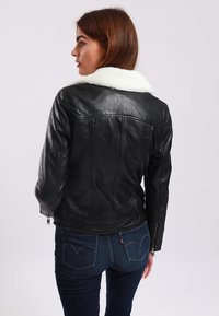 Black leather jacket with a white shearling collar. Features fitted design, zippered cuffs, and subtle stitching details.