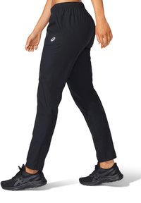 Black athletic pants with an elastic waistband, slim fit, and side pockets, paired with black running shoes featuring textured surfaces.