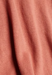 Tejido suave de color coral con una textura de punto fino. El material parece ligero, se drapea suavemente y presenta variaciones sutiles en la tonalidad.
