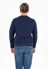 Felpa girocollo blu navy con polsini e orlo a costine, realizzata in materiale morbido; abbinata a jeans in denim blu con tasche posteriori.