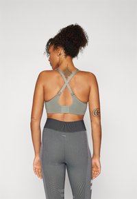 Top desportivo em verde suave com alças cruzadas nas costas e ganchos ajust�áveis, combinado com leggings cinzas texturizadas com riscas verticais.