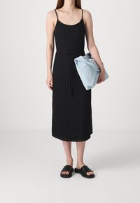 Černé bezramínkové šaty se strukturovaným vzorem a páskem v pase, v kombinaci se světle modrou taškou a černými sandály.