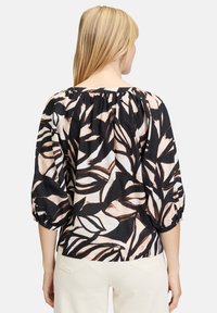 Blusa nera con un motivo floreale nei toni beige e crema. Presenta un collo arricciato e maniche a 3/4 con polsini elasticizzati. Tessuto leggero.