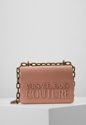 Rektangulær støvet pink lædertaske med stor præget "Versace Jeans Couture" tekst og en chunky guldkæde rem, der hviler på en hvid overflade.