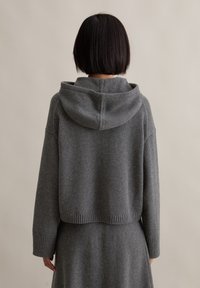 Grauer gestrickter Hoodie mit lässiger Passform, ribbeltem Saum und Bündchen, weicher Textur und verstellbarem Kapuzen. Von hinten getragen.