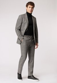 Completo a quadri grigio con vestibilità slim, caratterizzato da un blazer strutturato e pantaloni affusolati, abbinato a un dolcevita nero e sneakers nere.