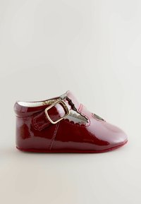 Błyszczące czerwone lakierowane buty ze sprzączką, z falistymi wycięciami, wyściełanym wnętrzem i miękką podeszwą, zaprojektowane dla niemowląt.