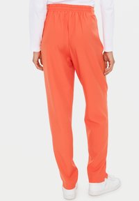 Helle orange Jogginghose mit elastischem Bund, geradem Bein und Seitentaschen, kombiniert mit weißen Turnschuhen.