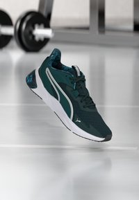 Dark green athletic shoe with a textured upper, white midsole, and patterned accents on the heel. Features laces and a logo.