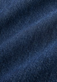 Gros plan d'un tissu en denim bleu foncé montrant un tissage texturé et de légers plis.