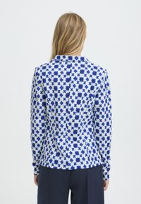 Chemise à manches longues présentant un motif d'étoiles bleu et blanc, confectionnée dans un tissu doux à la texture lisse avec un col classique.