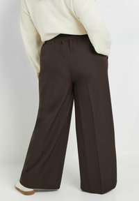 Bruine wijde broek van geweven stof met een elastische tailleband, voorzien van zijzakken en een losse pasvorm voor comfort.
