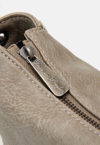 Beżowe botki na kostkę z imitacji skóry z metalowym zamkiem błyskawicznym i wyciętym uchwytem, z widocznymi szwami i lekko teksturowaną powierzchnią.