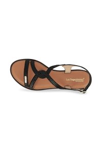 Sandalia negra con diseño de tiras cruzadas, parte superior de textil texturizado, plantilla en tono bronceado y un pequeño acento de logo dorado. Suela plana, correa ajustable en el tobillo.