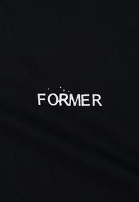 Μαύρο βαμβακερό t-shirt με το κείμενο «FORMER» σε λευκό, με ένα ελαφρώς φθαρμένο εφέ στα γράμματα. Ομαλή υφή.