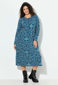 Vestido de manga larga y longitud hasta la rodilla en azul con un patrón floral, que presenta acentos en blanco y azul verdoso. Combinado con botas de combate negras.