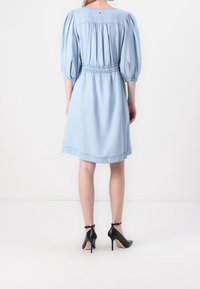 Hellblaues Denim-Kleid mit Puffärmeln, elastischem Bund und knielanger Säume. Ein Paar schwarze High Heels mit Knöchelriemen.