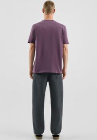 Męski krótki rękaw, koszulka z okrągłym dekoltem w głębokim fiolecie, zestawiona z luźnymi ciemnoszarymi dżinsami. Prosty design, bawełniany materiał, bez widocznych wzorów.