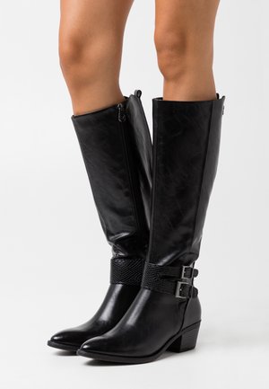 Mustat polven korkeuteen ulottuvat saappaat, jotka on valmistettu sileästä keinonahasta. Niissä on kaksi sivuvetoketjua, teksturoidut mustat remmit hopeisilla soljilla ja matala korko.